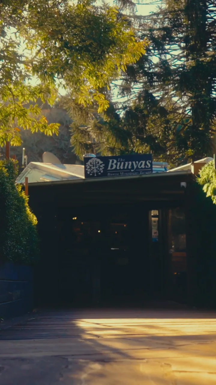 The Bunyas tavern entrance and sign framed by trees in warm sunlight.